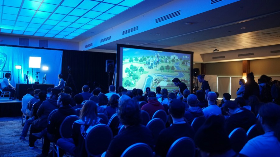 Audience in a blue-lit hall watching a presentation at an annual meeting